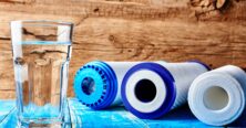 Water filters. Carbon cartridges and a glass of water on a wooden background. Household filtration system.